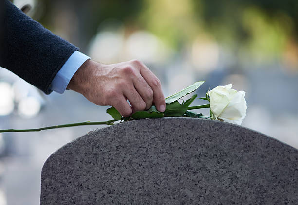 Cropped shot of a man placing a white rose on a grave two people sitting during day